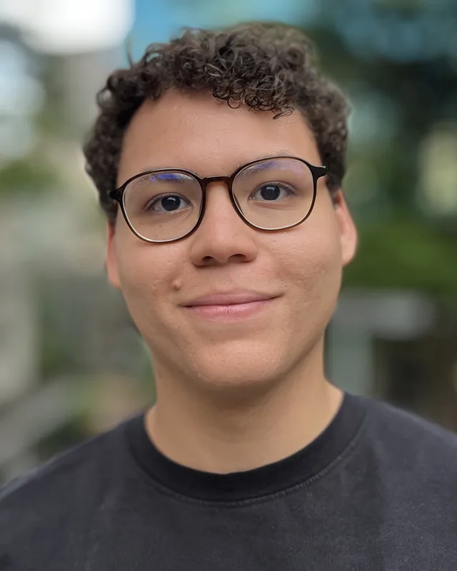 Gabriel Lacerda, de óculos e camiseta escura, sorrindo ao ar livre